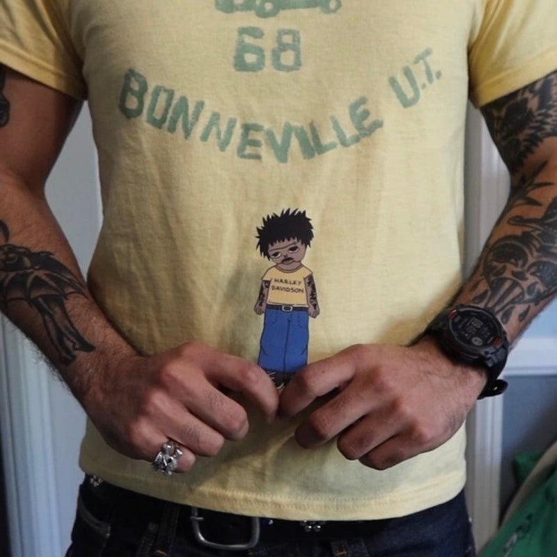 Person wearing a yellow t-shirt with text and a graphic design, standing indoors.